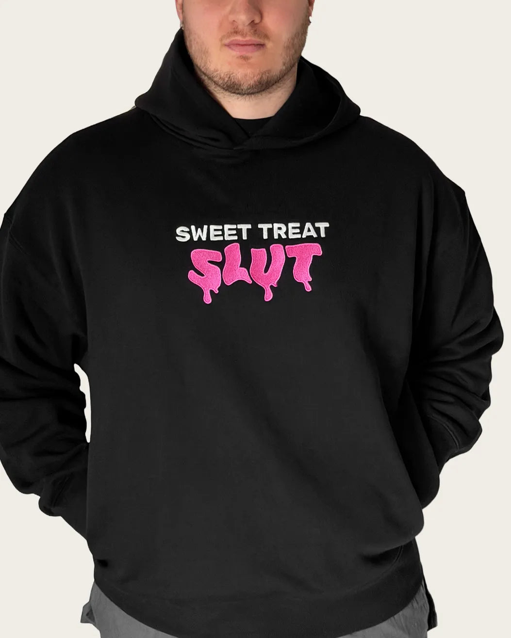 Close up of man wearing black embroidered hoodie with text 'sweet treat slut'.