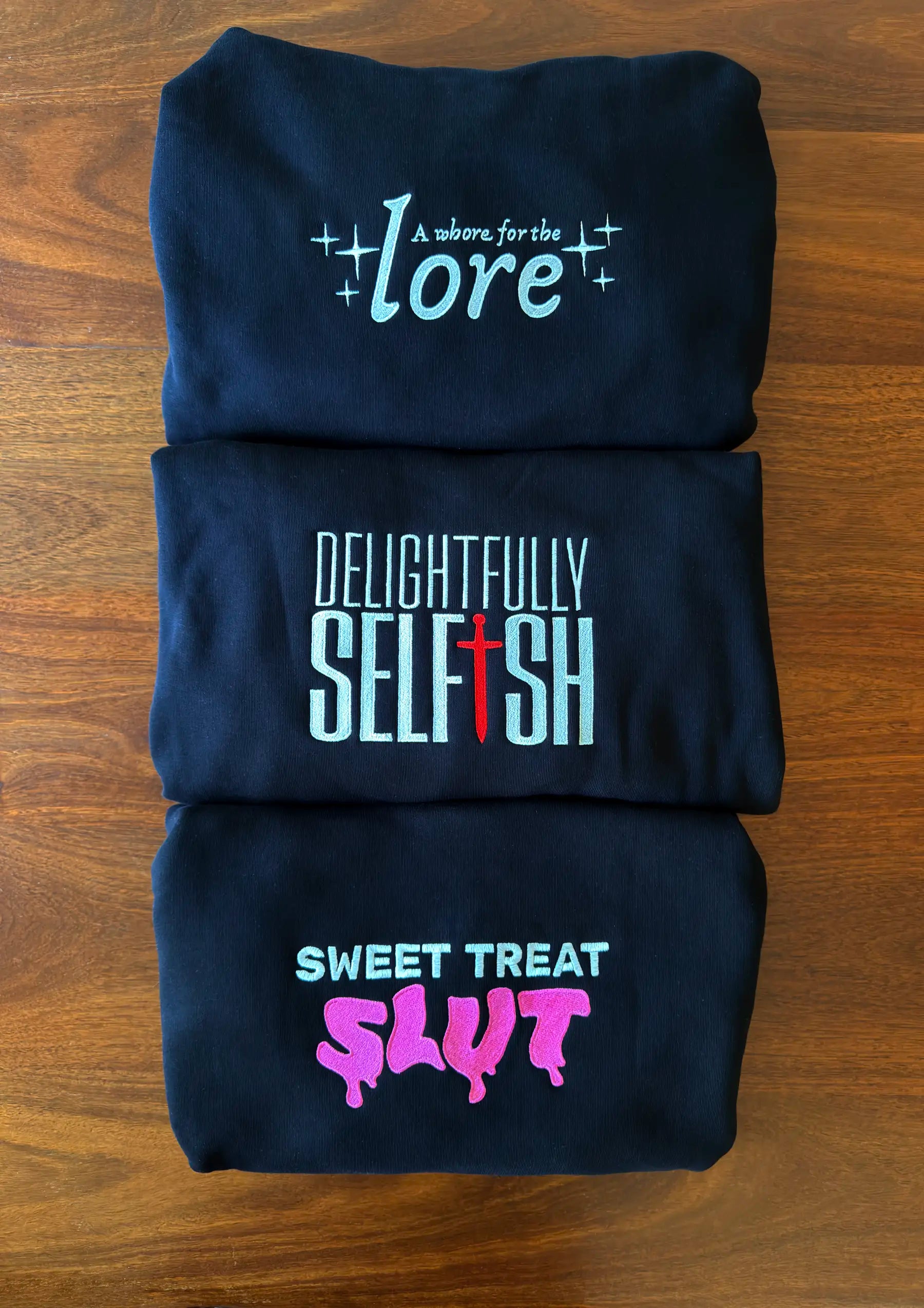 stack of black hoodies with embroidered text on a wood background