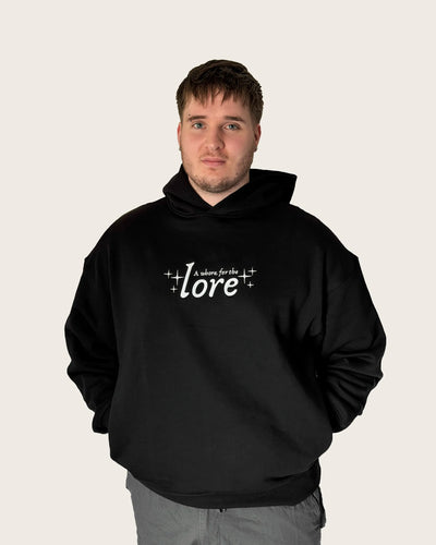 Man wearing oversized black hoodie with embroidered text 'a whore for the lore'.