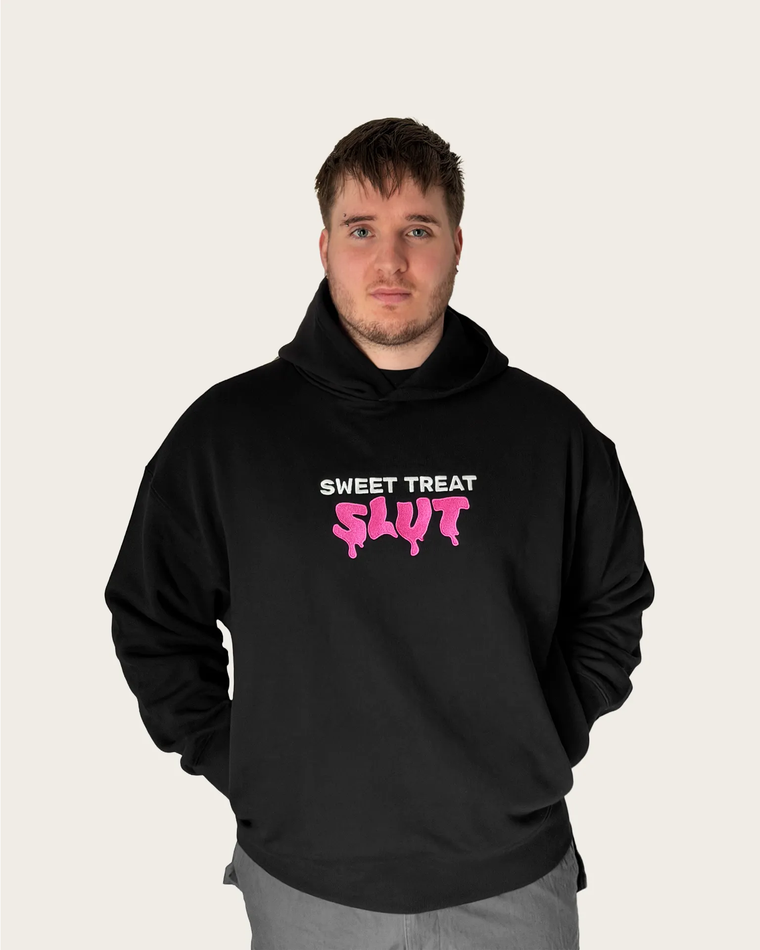 Man wearing black embroidered hoodie with text 'sweet treat slut'.